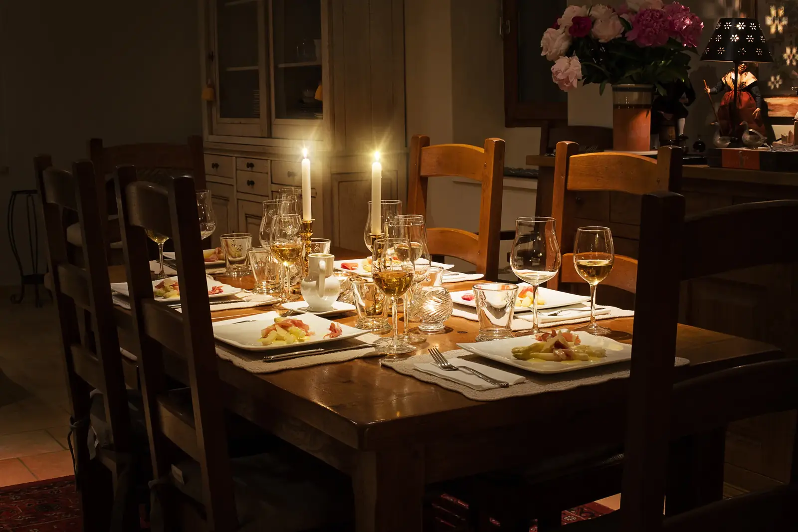 A candlelit wooden dining table set with plates and glasses in a warm, dark room