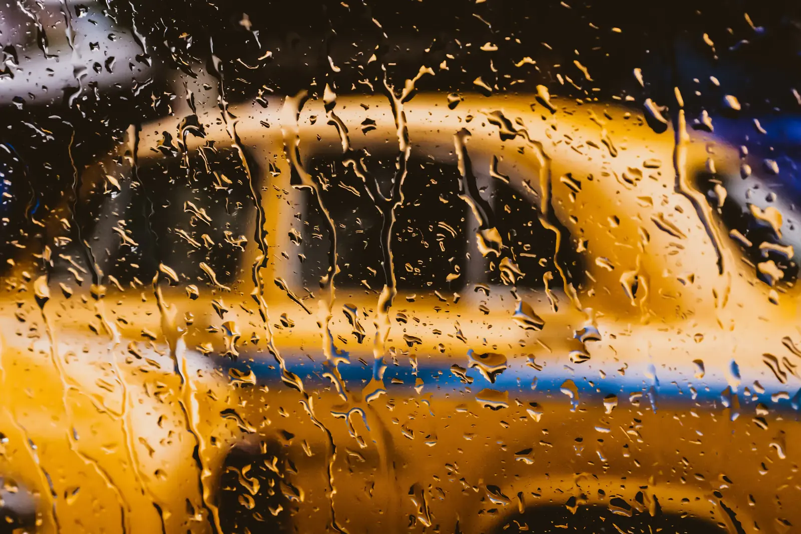 A yellow cab blurred through rain on glass