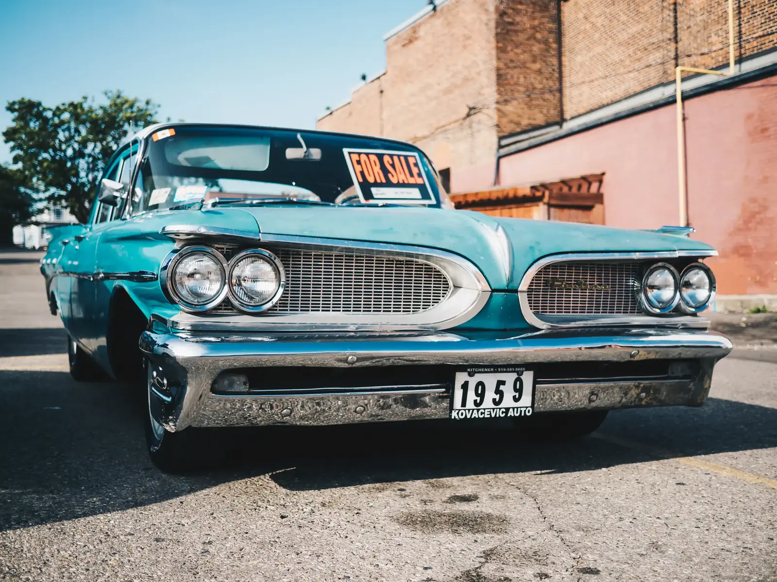 A turquoise 1950s car parked by a brick wall in bright sun