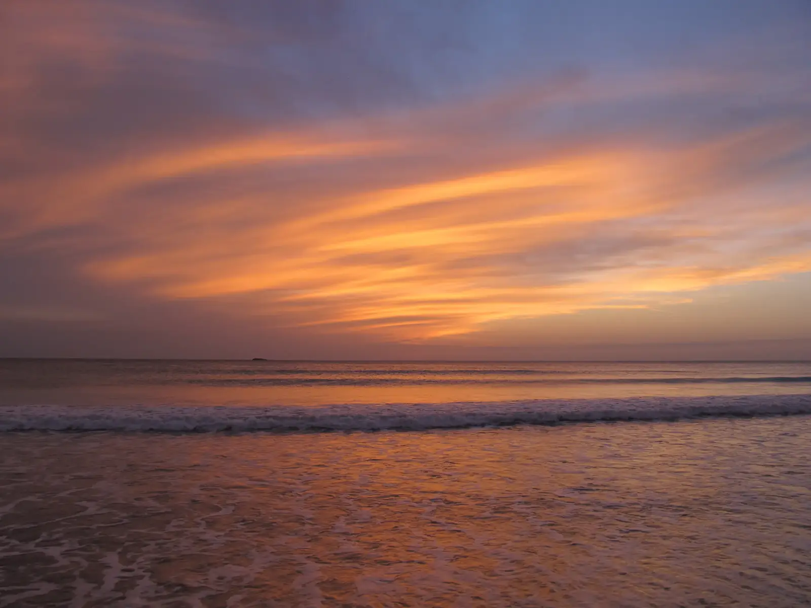 Foamy waves rolling in under an orange sunset