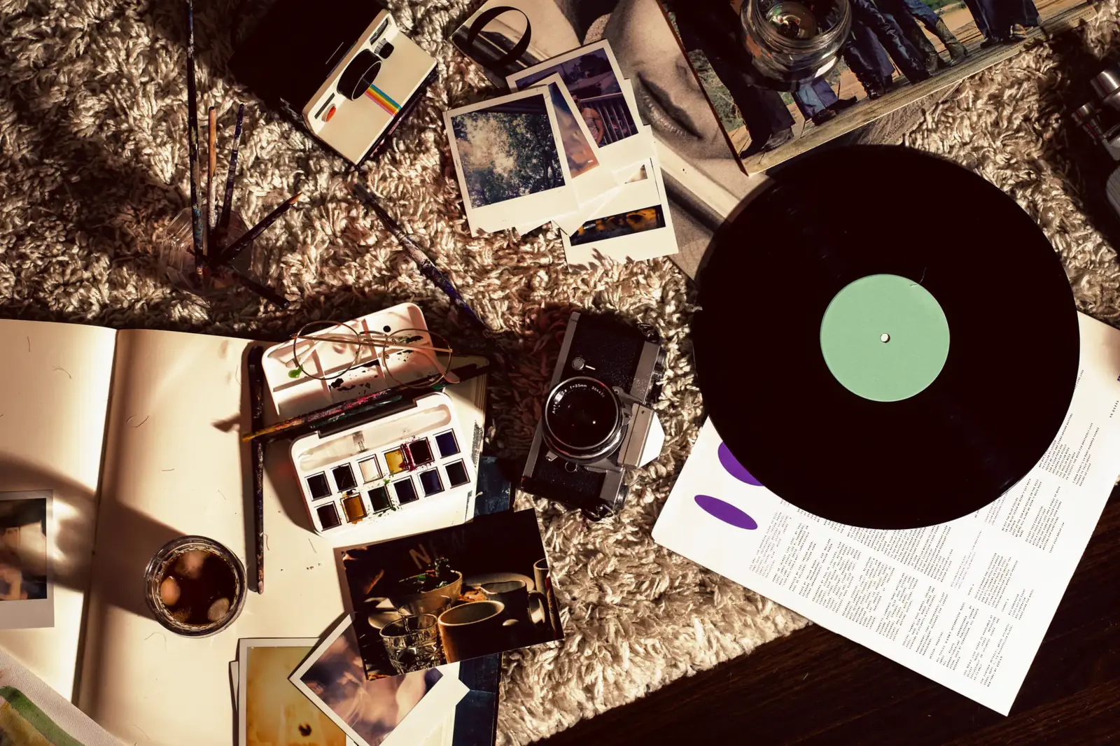 A vinyl record, Polaroids and old cameras scattered on a rug