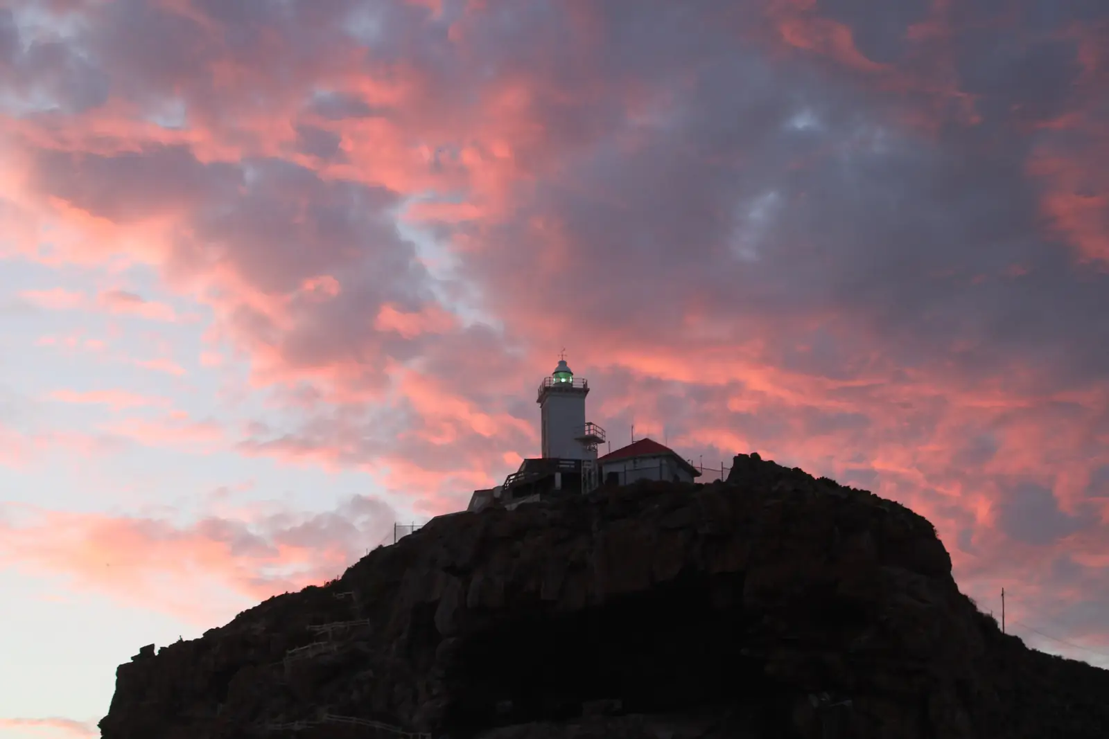 A lighthouse on a dark headland under pink clouds