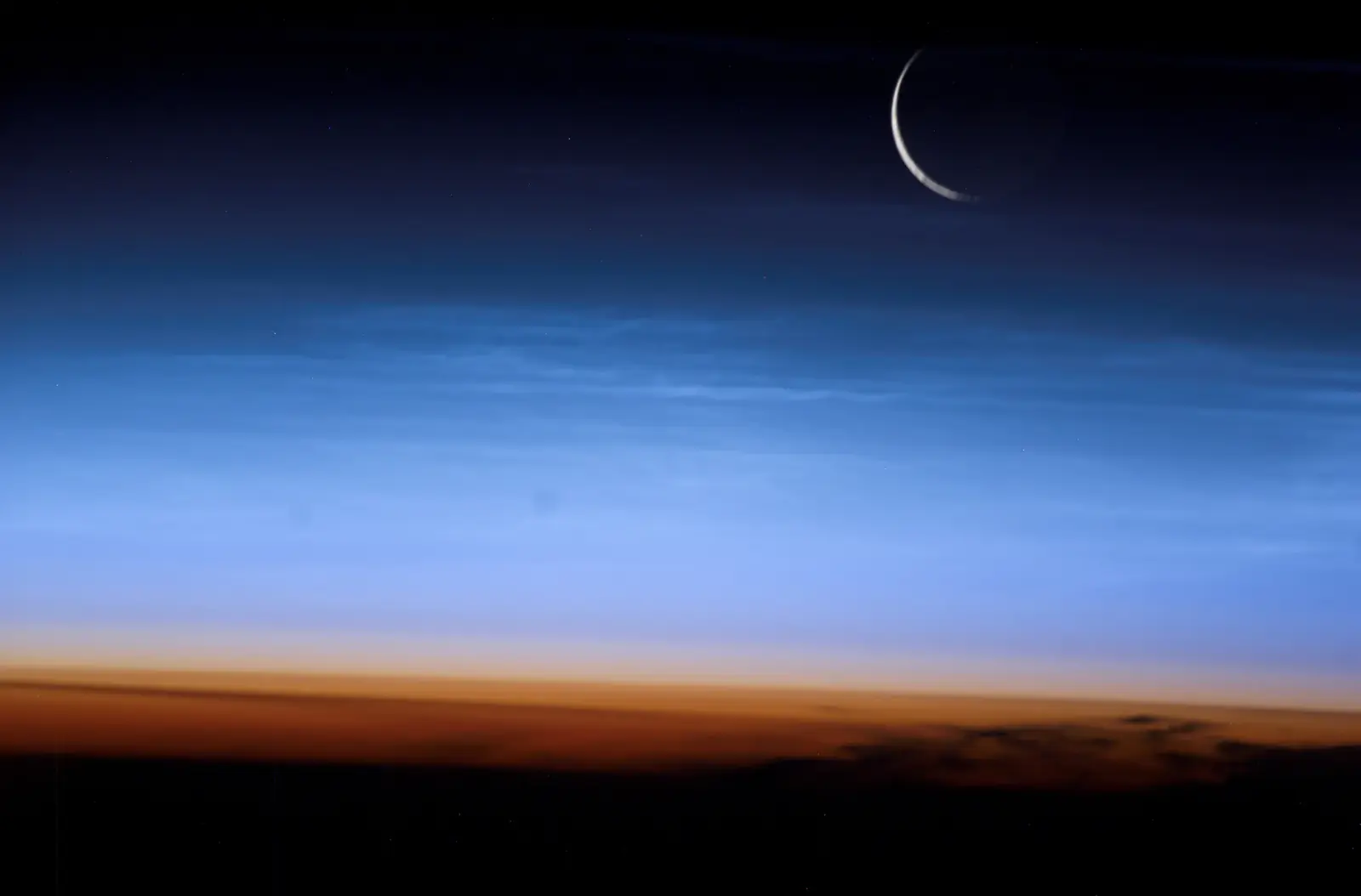 A thin crescent Moon above the glowing blue layers of Earth's atmosphere, seen from orbit