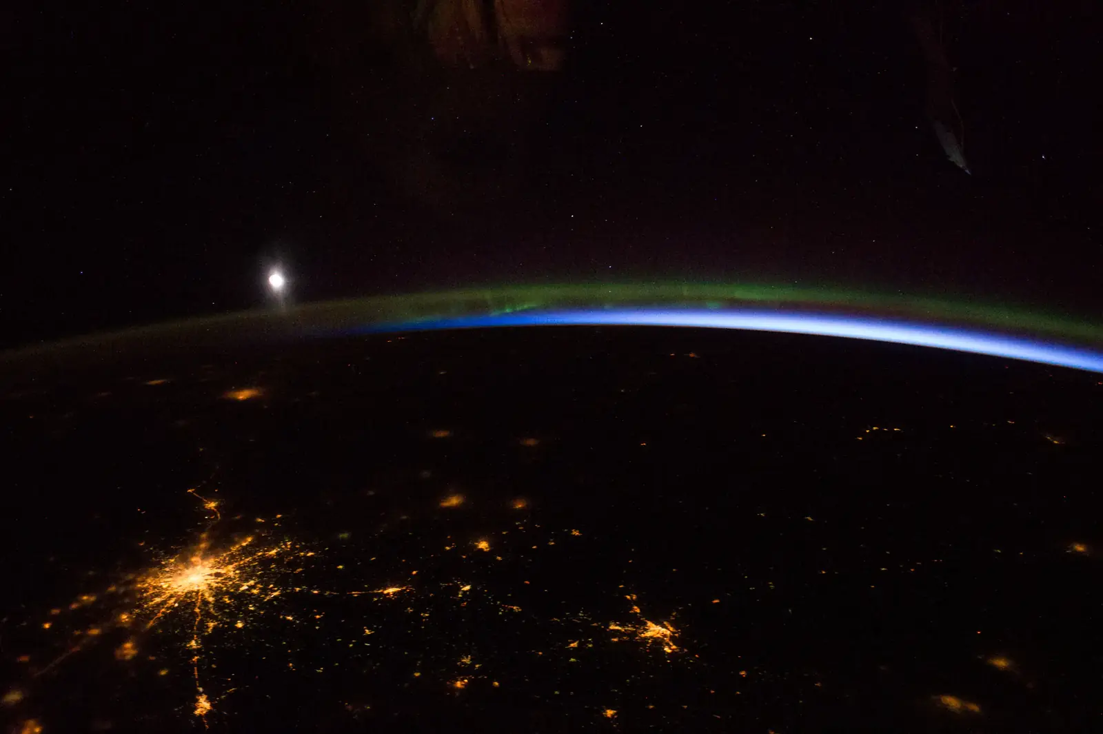 City lights, an aurora and the Moon over the Earth's curve, seen from orbit
