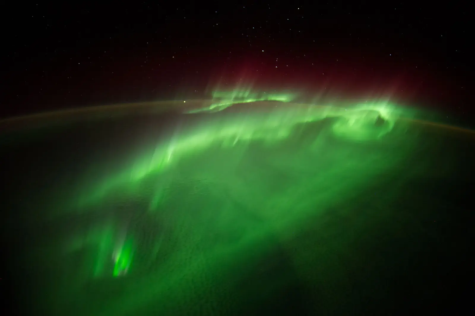 A green aurora swirling over the night side of the Earth, seen from the International Space Station