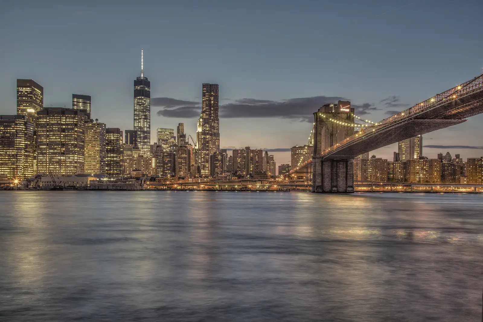 A city skyline and bridge lit up across the water at dusk