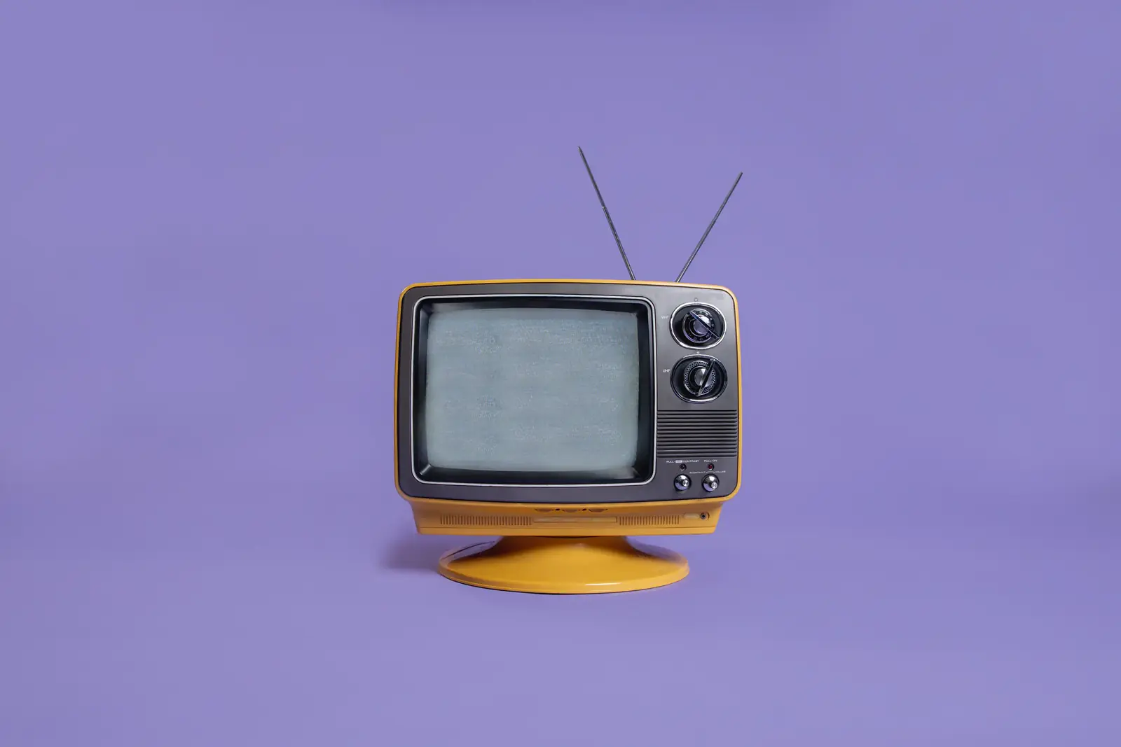 A yellow vintage television with rabbit-ear antennas on a lilac background