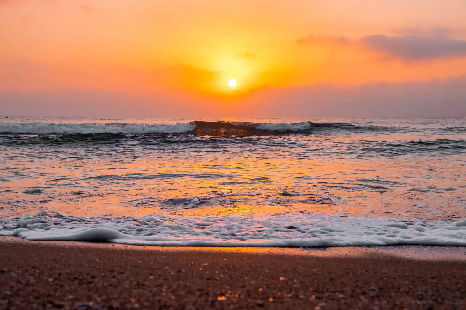 The sun rising over waves breaking on a sandy beach