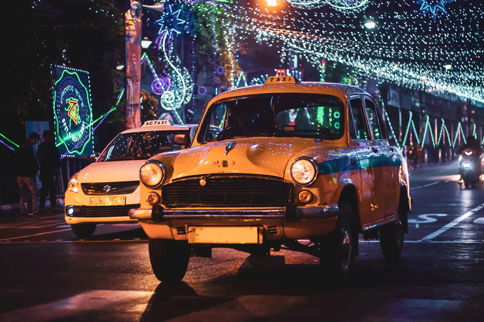 A vintage yellow taxi on a street strung with festival lights