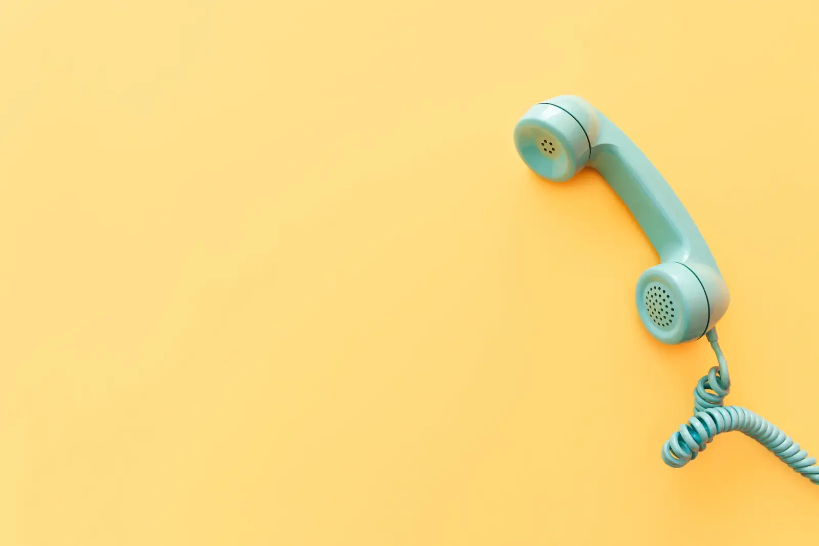 A mint telephone receiver dangling against bright yellow