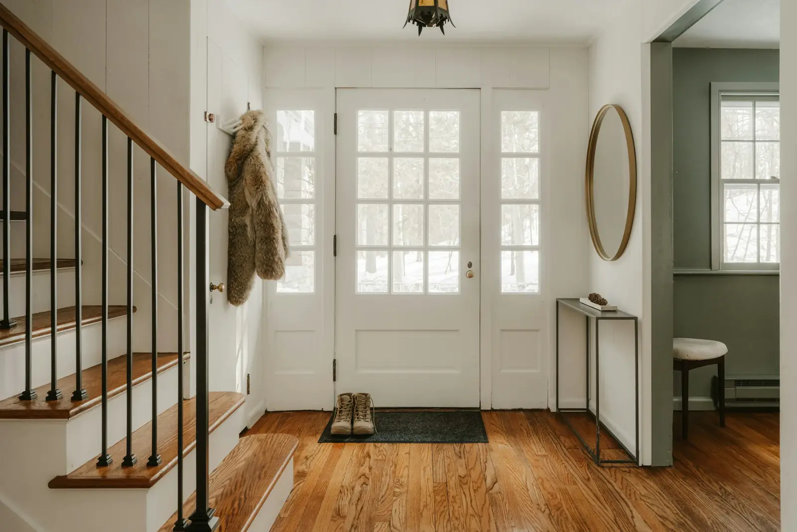A bright front hallway with a staircase, coats on hooks and a glass-panelled door