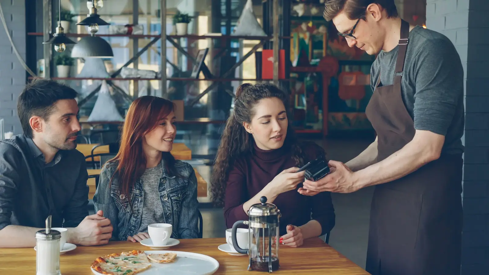 Friends at a café table as a waiter takes payment