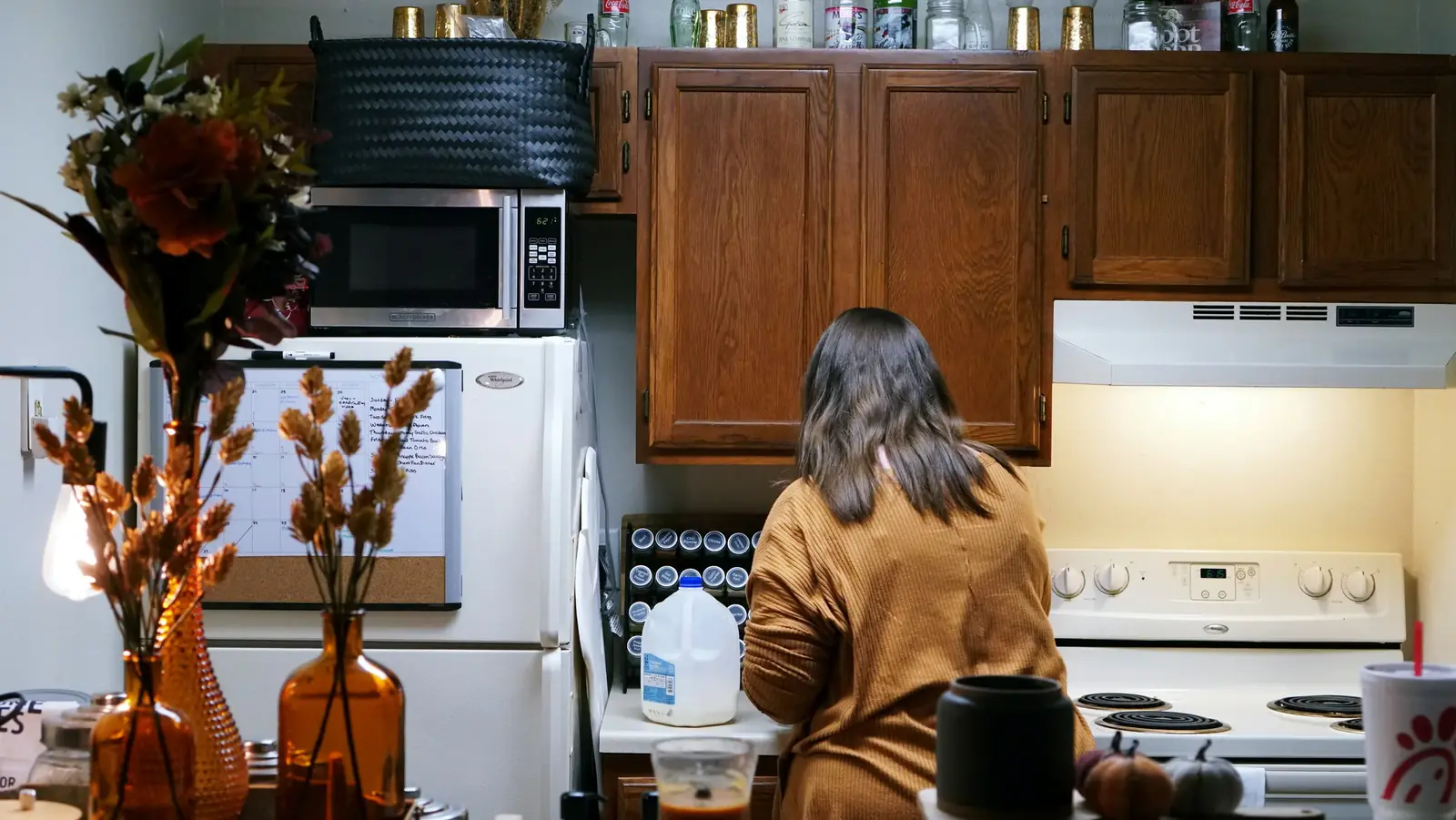 A woman cooks at the stove of a homely kitchen, dried autumn branches on the counter