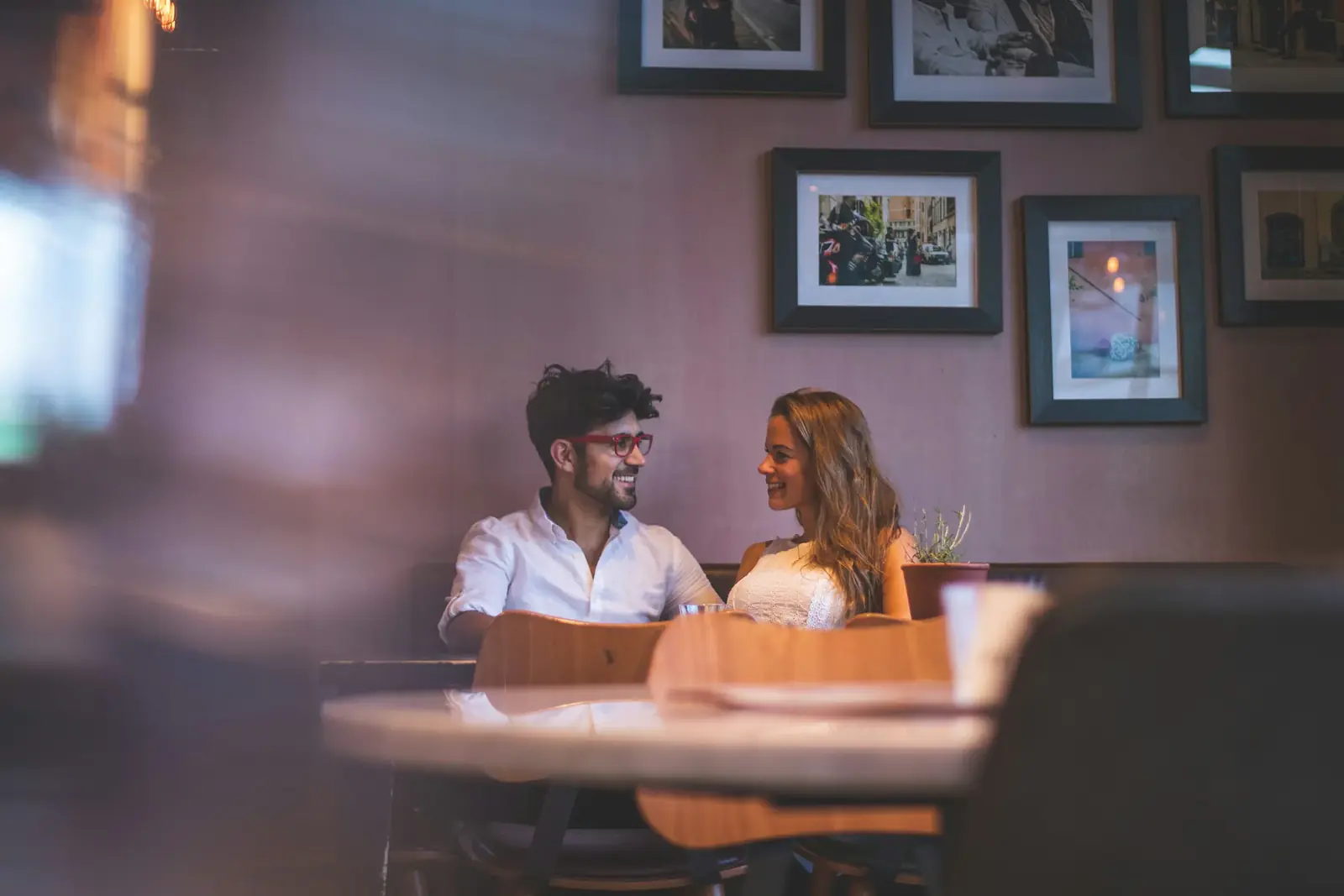 A couple talks across a small restaurant table, seen through a window