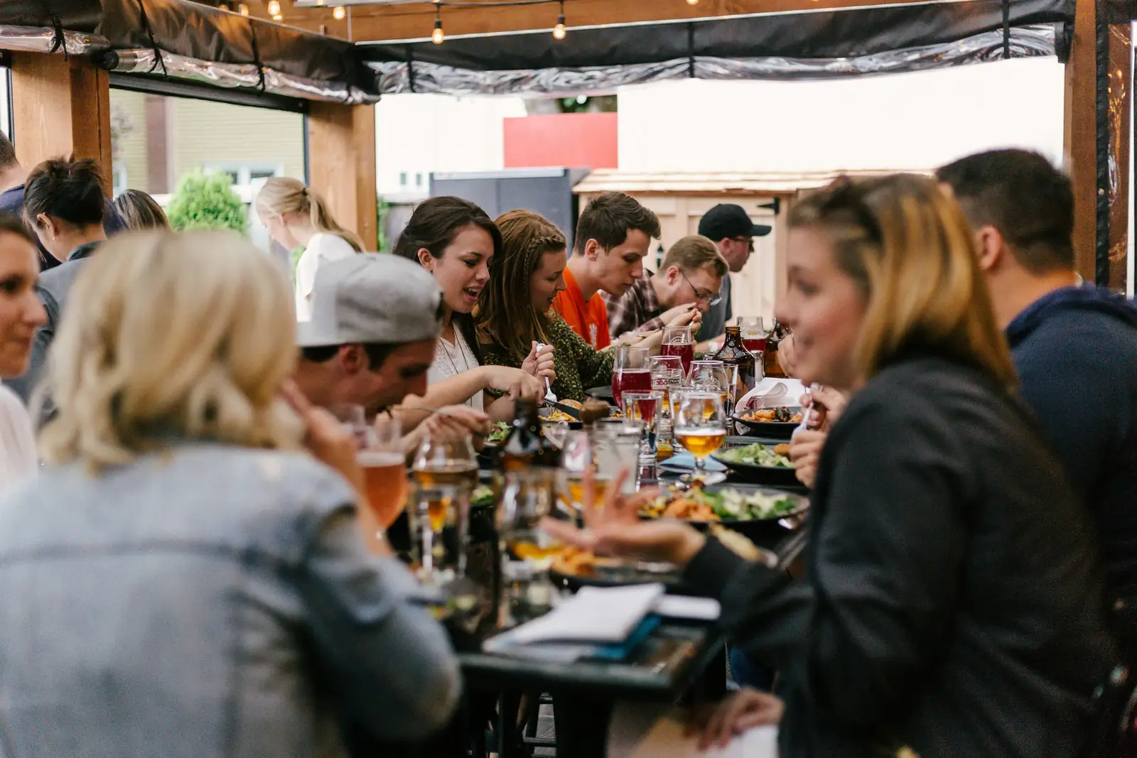 Friends talk and laugh around a long table crowded with dinner and drinks