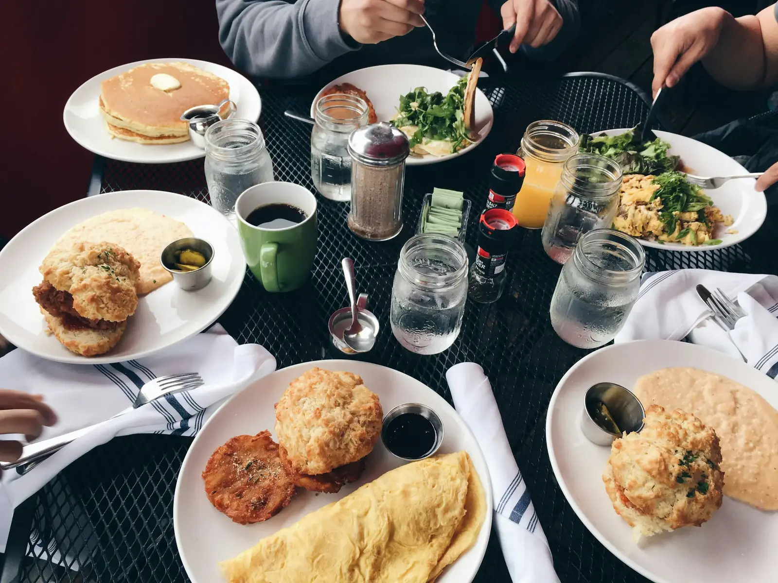 Plates of brunch, coffee and drinks crowd a shared café table