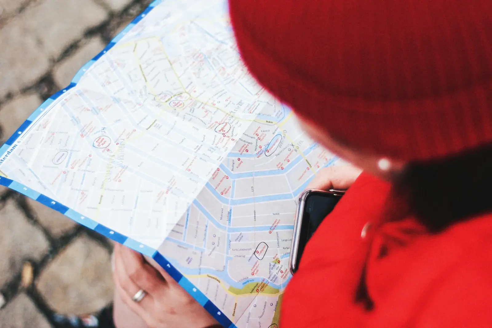 A person in a red beanie studies a paper street map of Amsterdam