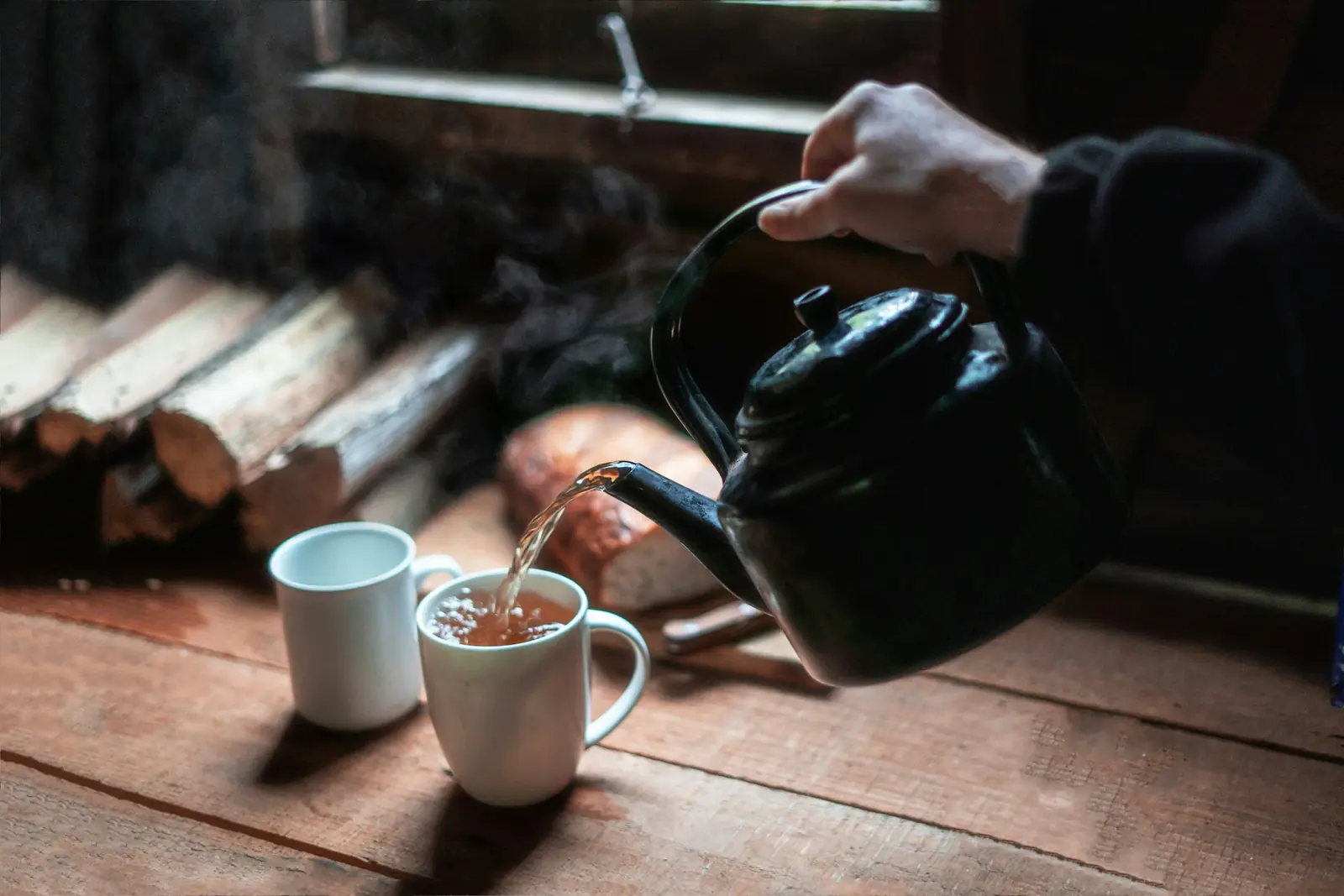 Tea poured from a black kettle into a white mug on a wooden table