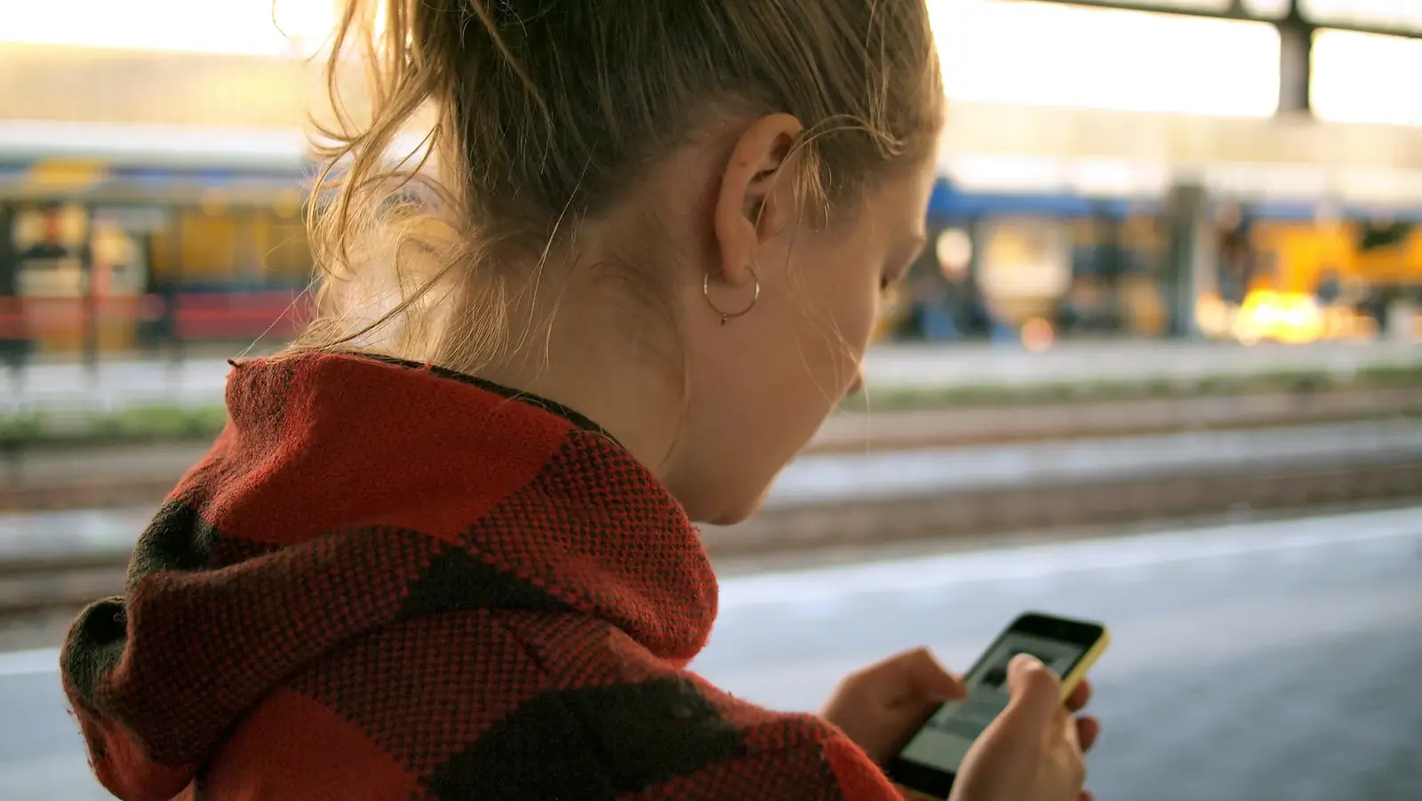 A woman in a red hoodie checks her phone on a train platform