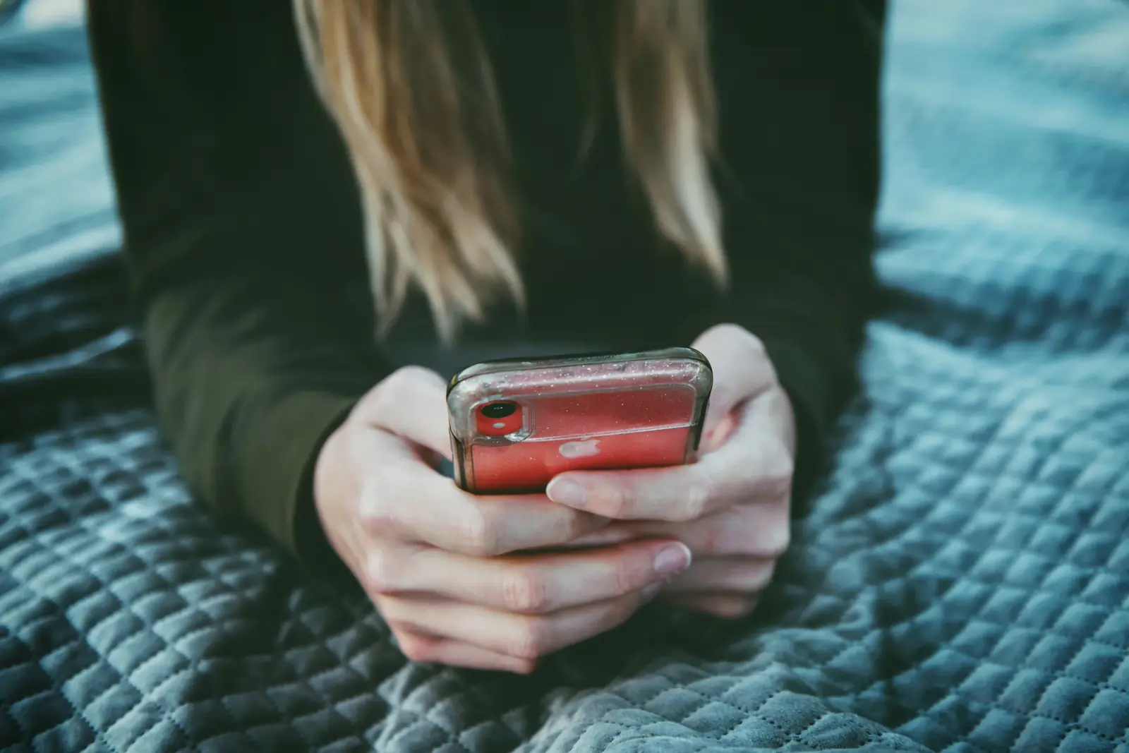 Hands hold a phone over a quilted blanket, mid-message