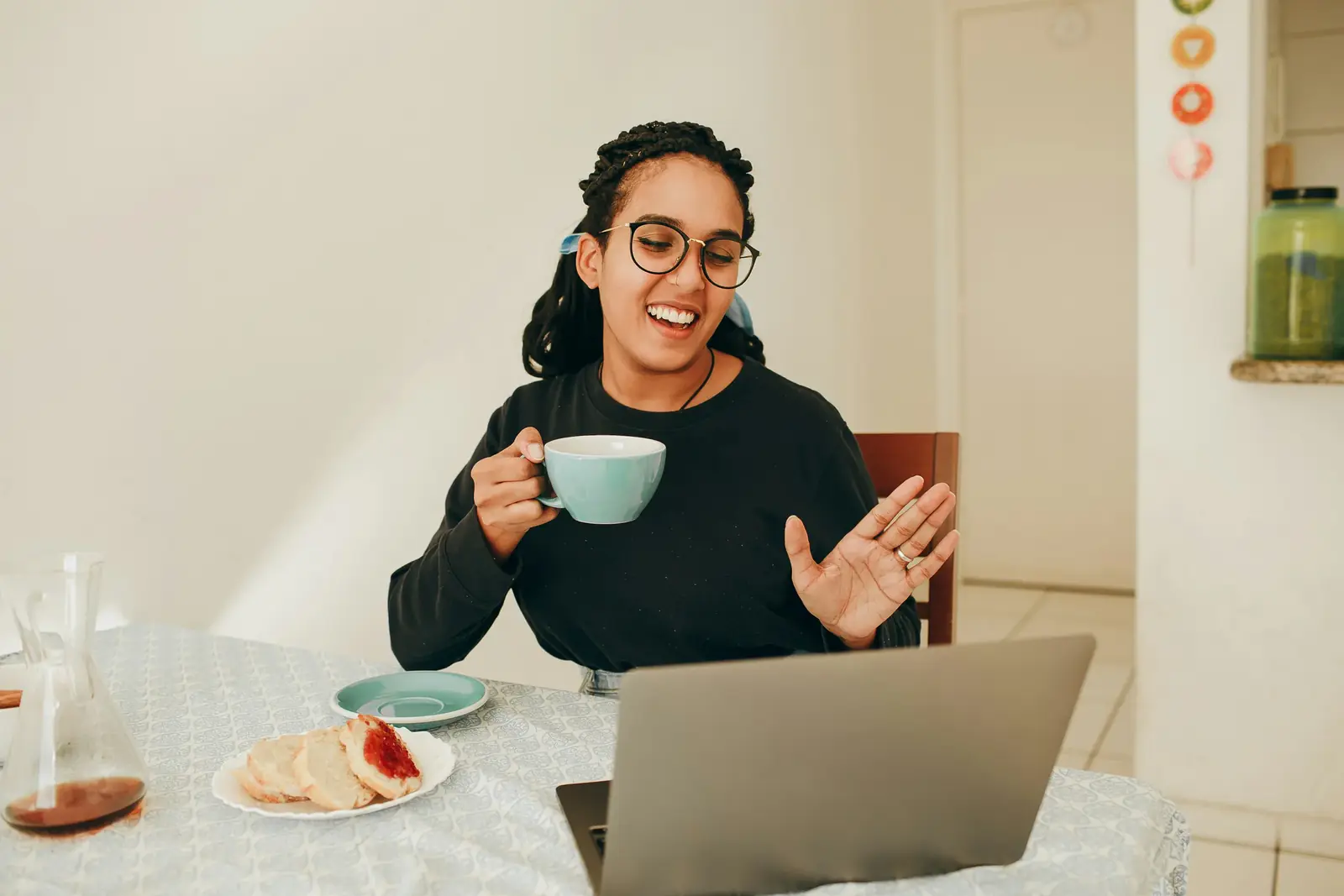 A woman with a cup of tea talks animatedly to a laptop on a video call