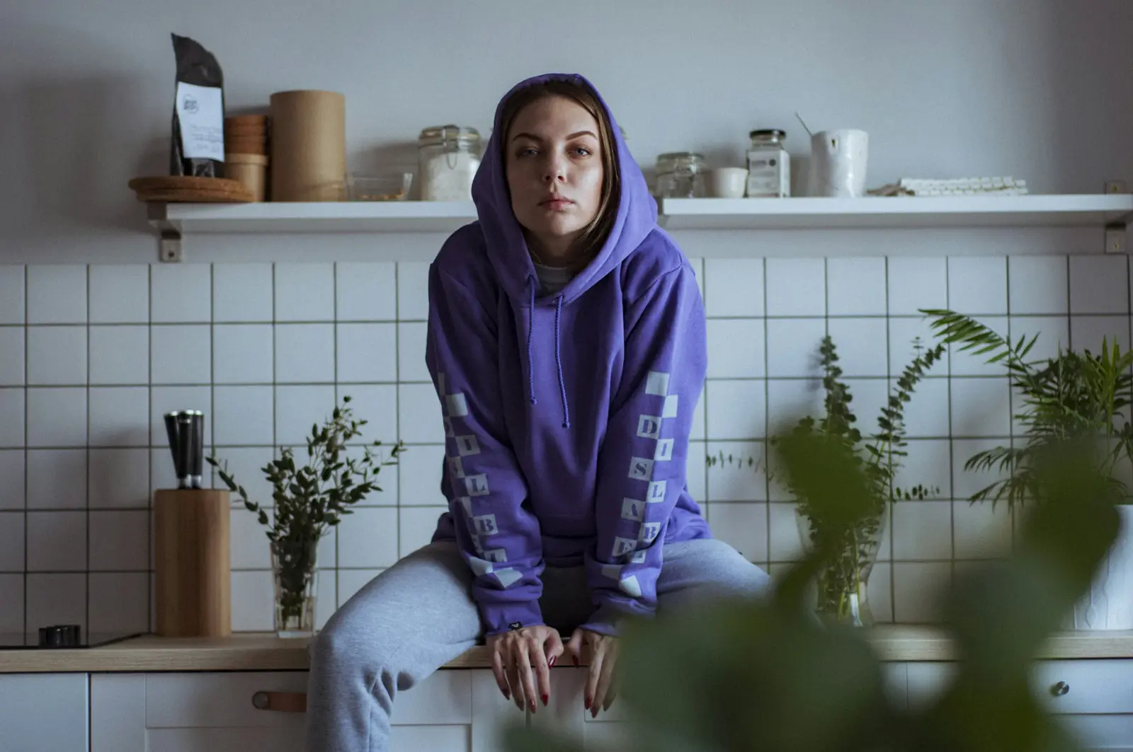 A woman in a purple hoodie sits on a kitchen counter, waking up slowly
