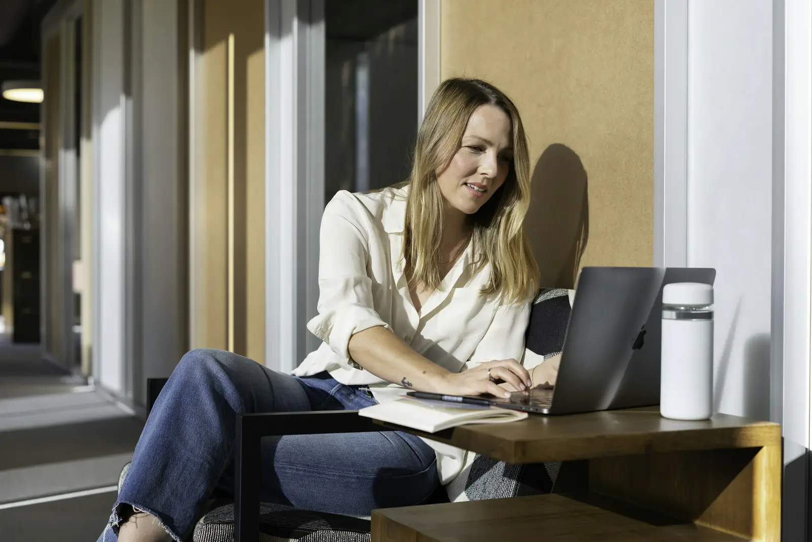 A woman works through papers on a laptop in a sunlit office
