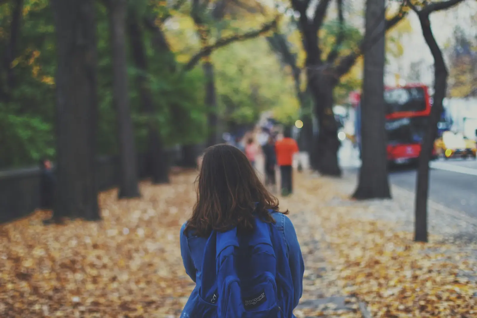 A woman in a blue jacket walks through fallen leaves in Central Park