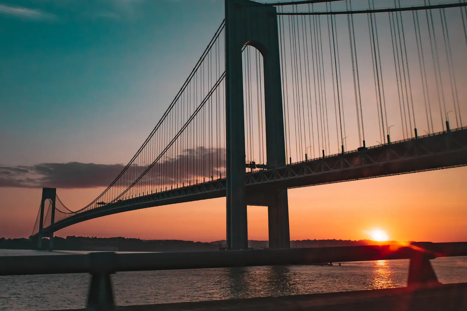A suspension bridge silhouetted against an orange sunset