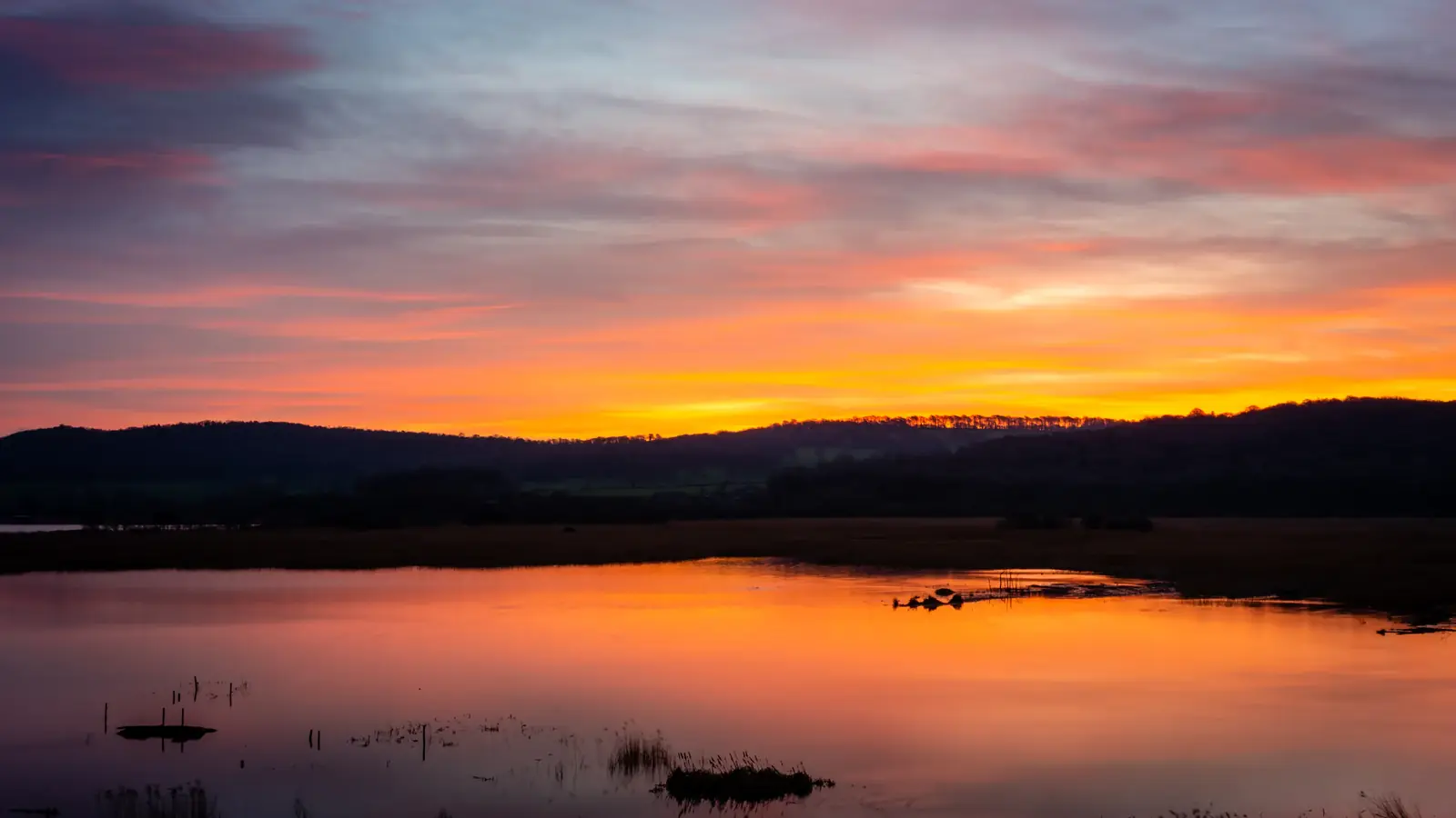 An orange and pink sunset mirrored in a still pond