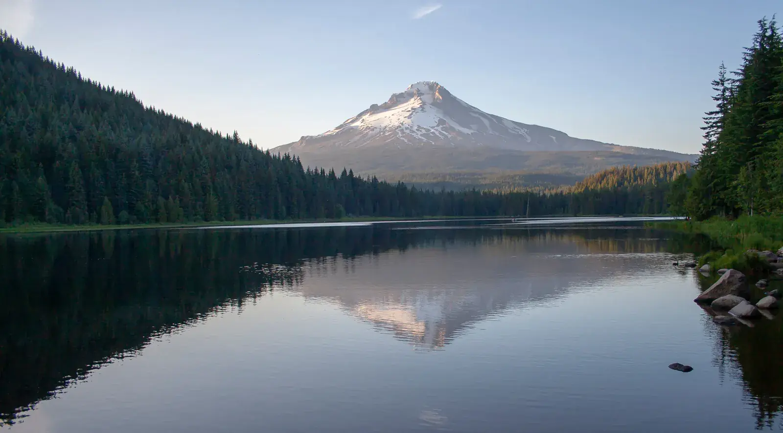 A snowy volcano mirrored in a still forest lake