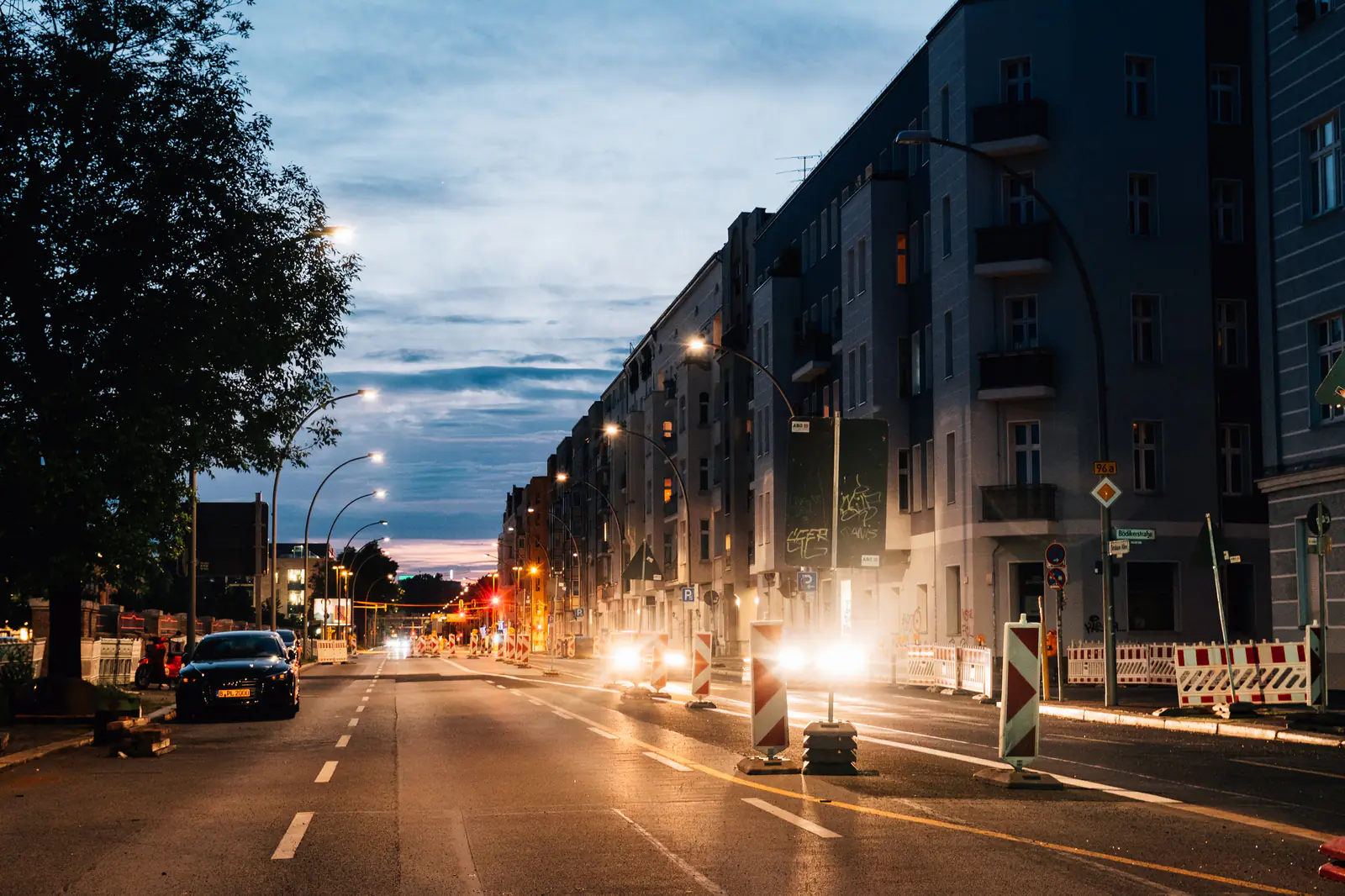 A city avenue at dusk with streetlights coming on