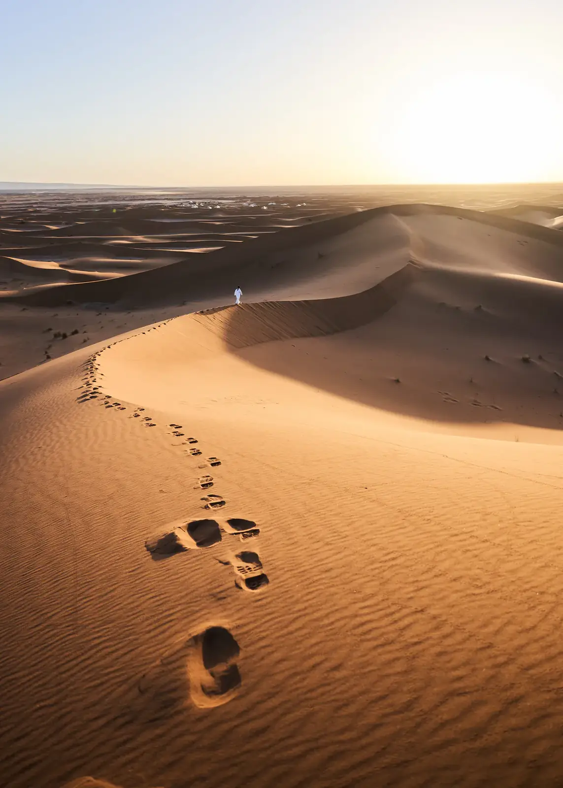 Footprints trailing over a sand dune toward the light