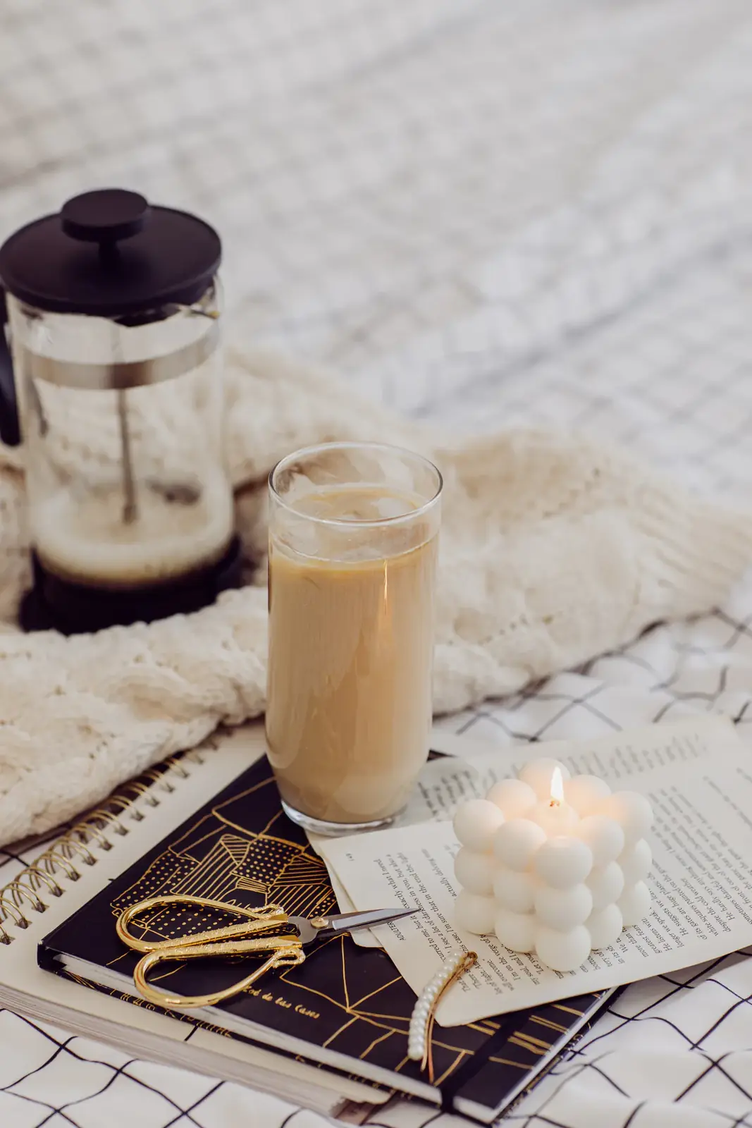 Iced coffee, a candle and a notebook on a cosy bed