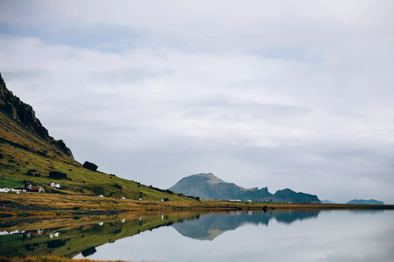 Green hills mirrored in a still lake under grey cloud