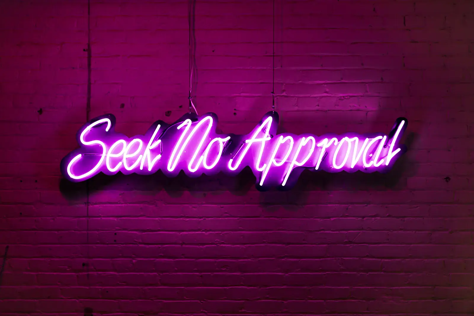 A pink neon sign reading "Seek No Approval" on a brick wall