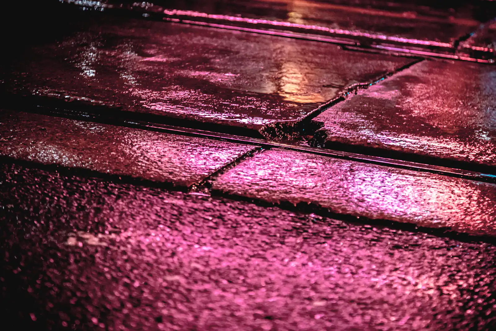 Pink neon reflected on a wet pavement at night