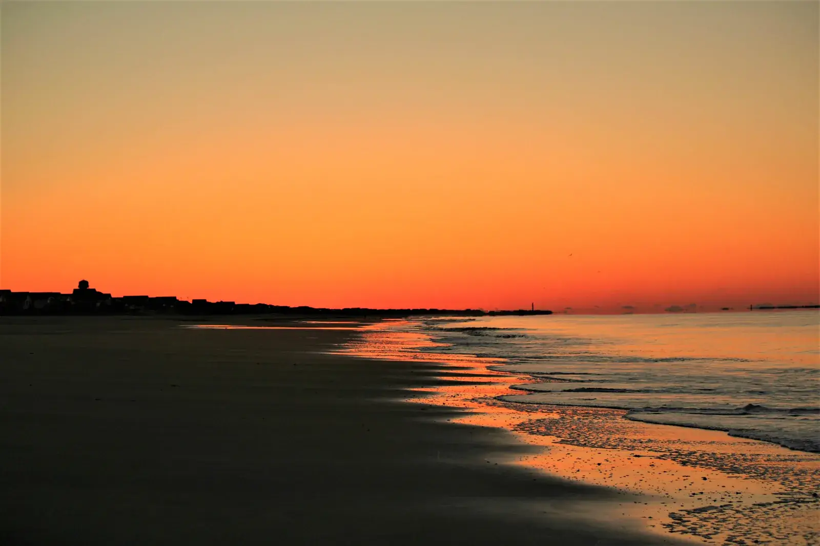 A blazing orange sunset over a wet beach