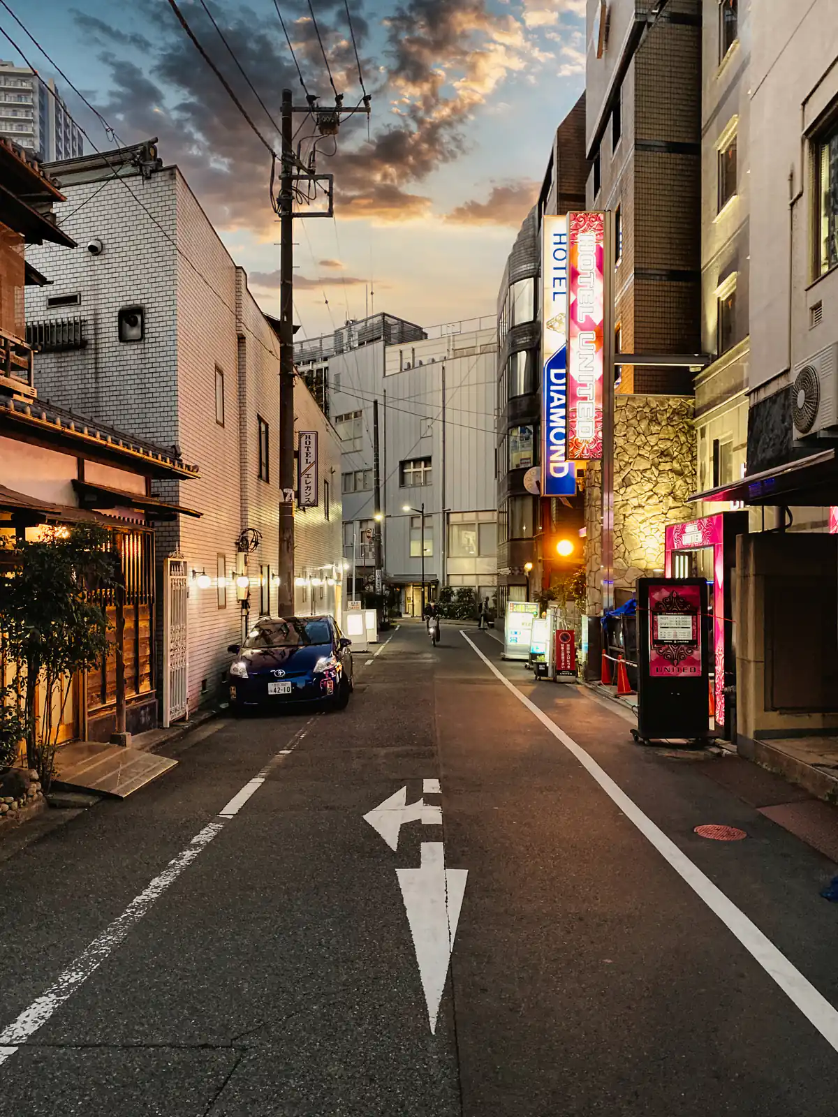 A narrow street of glowing signs at dusk