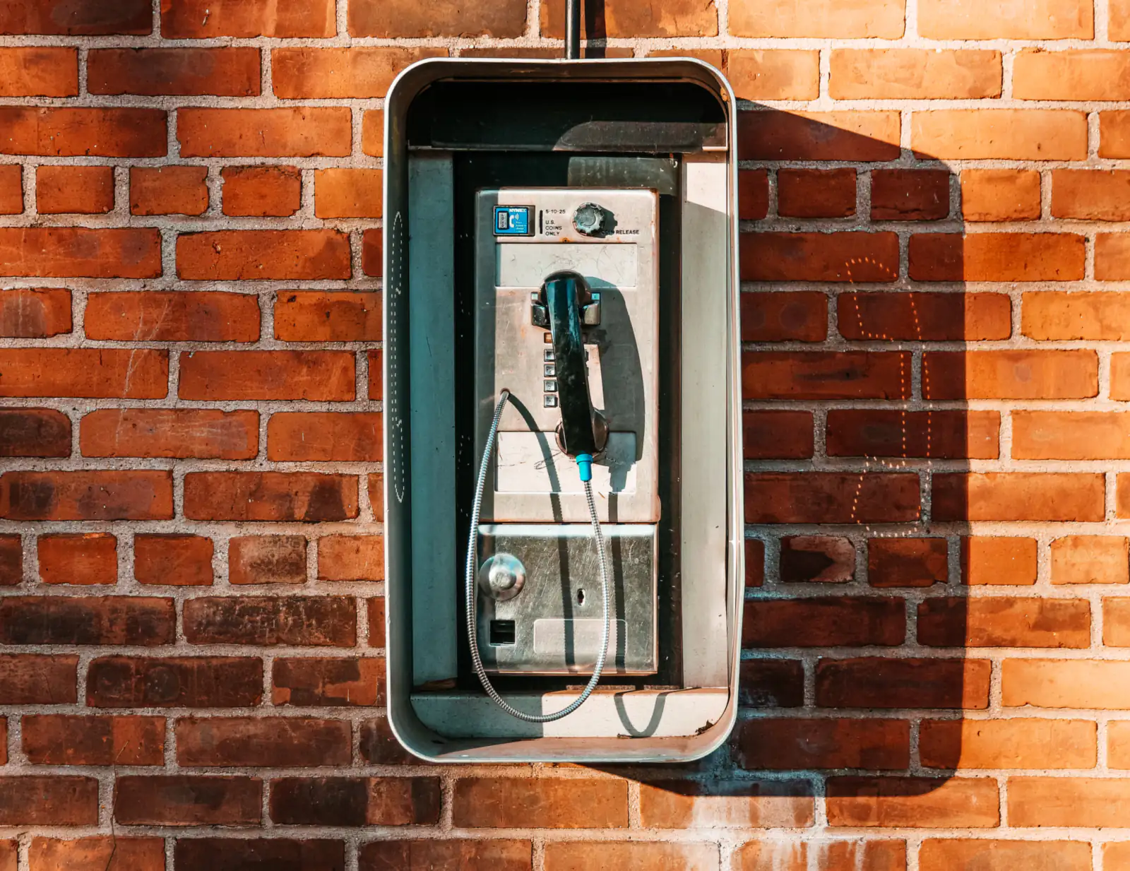 An old payphone on a sunlit red-brick wall