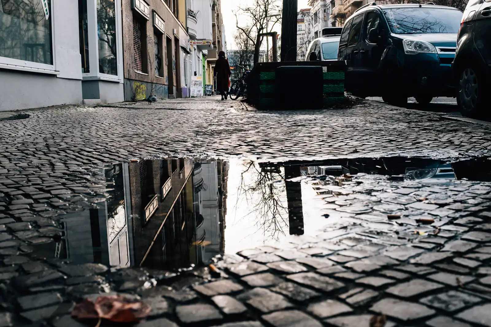A city street reflected in a puddle on cobblestones
