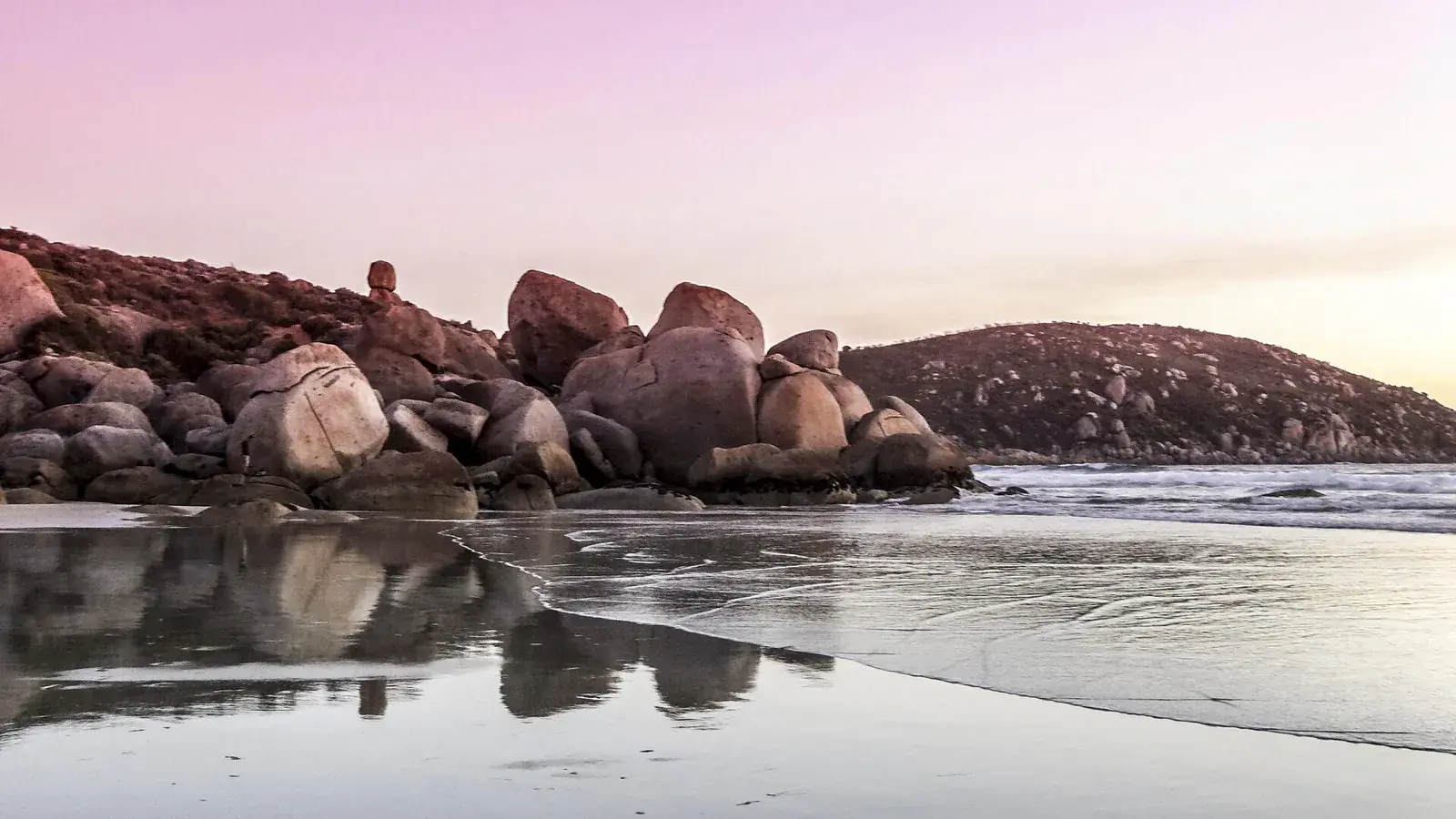 Pink-lit boulders mirrored in a wet beach