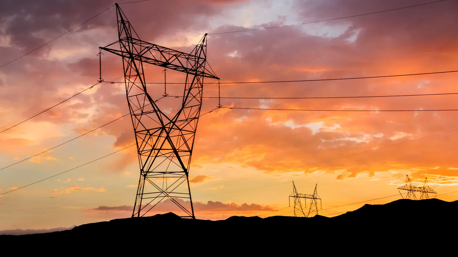 A power pylon against a blazing orange sky