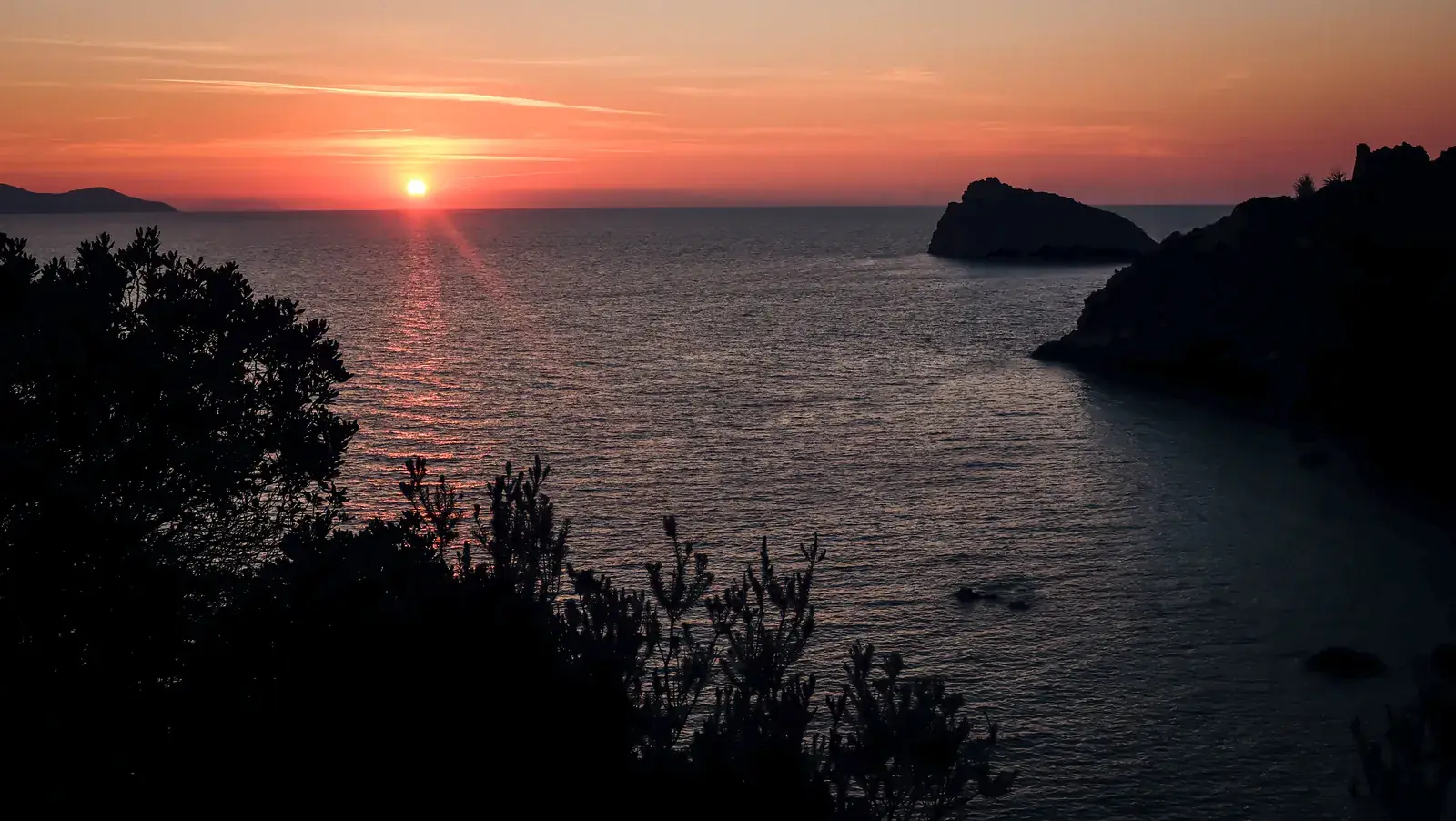 The sun setting into the sea beside a rocky headland