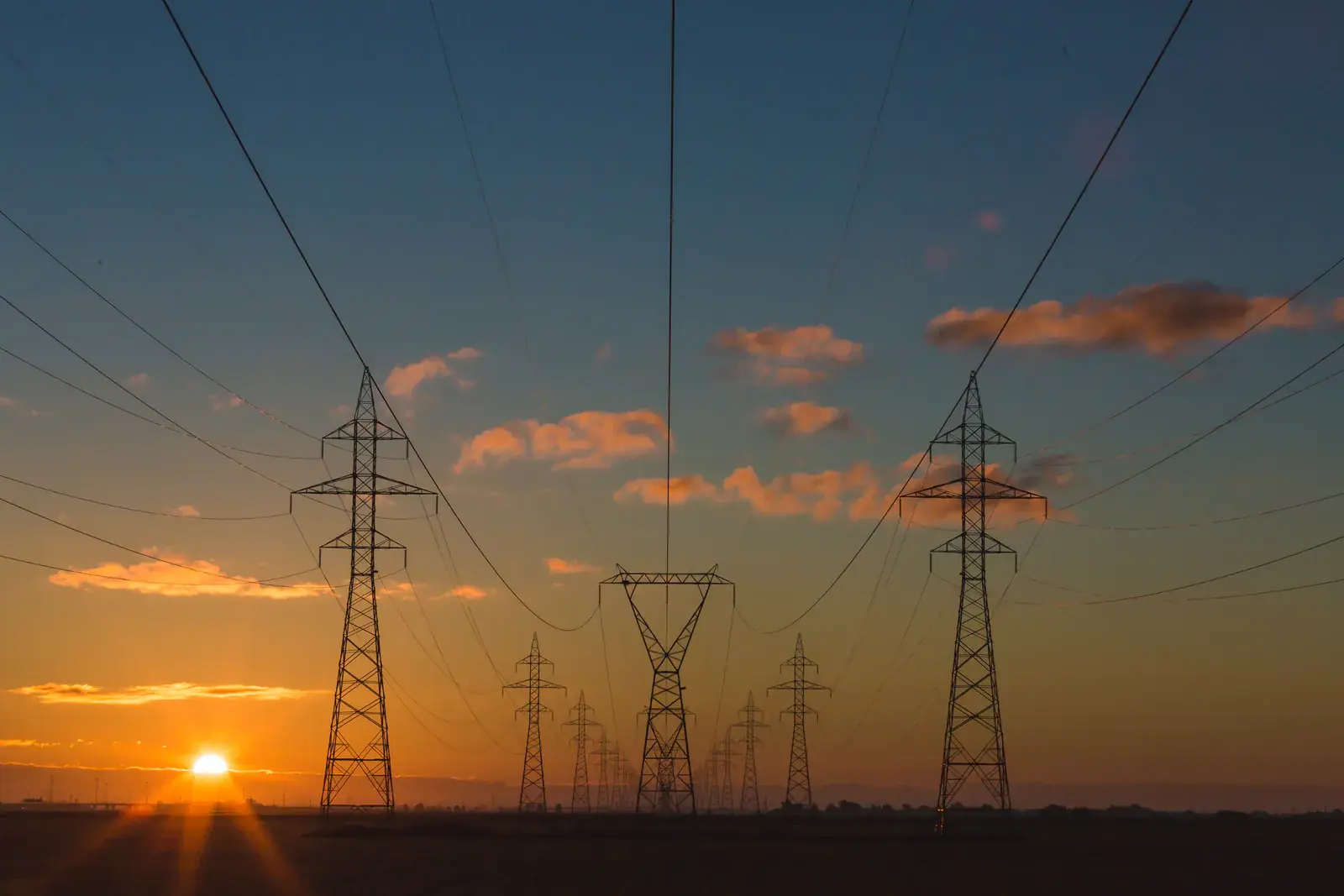 Power lines running toward an orange sunset