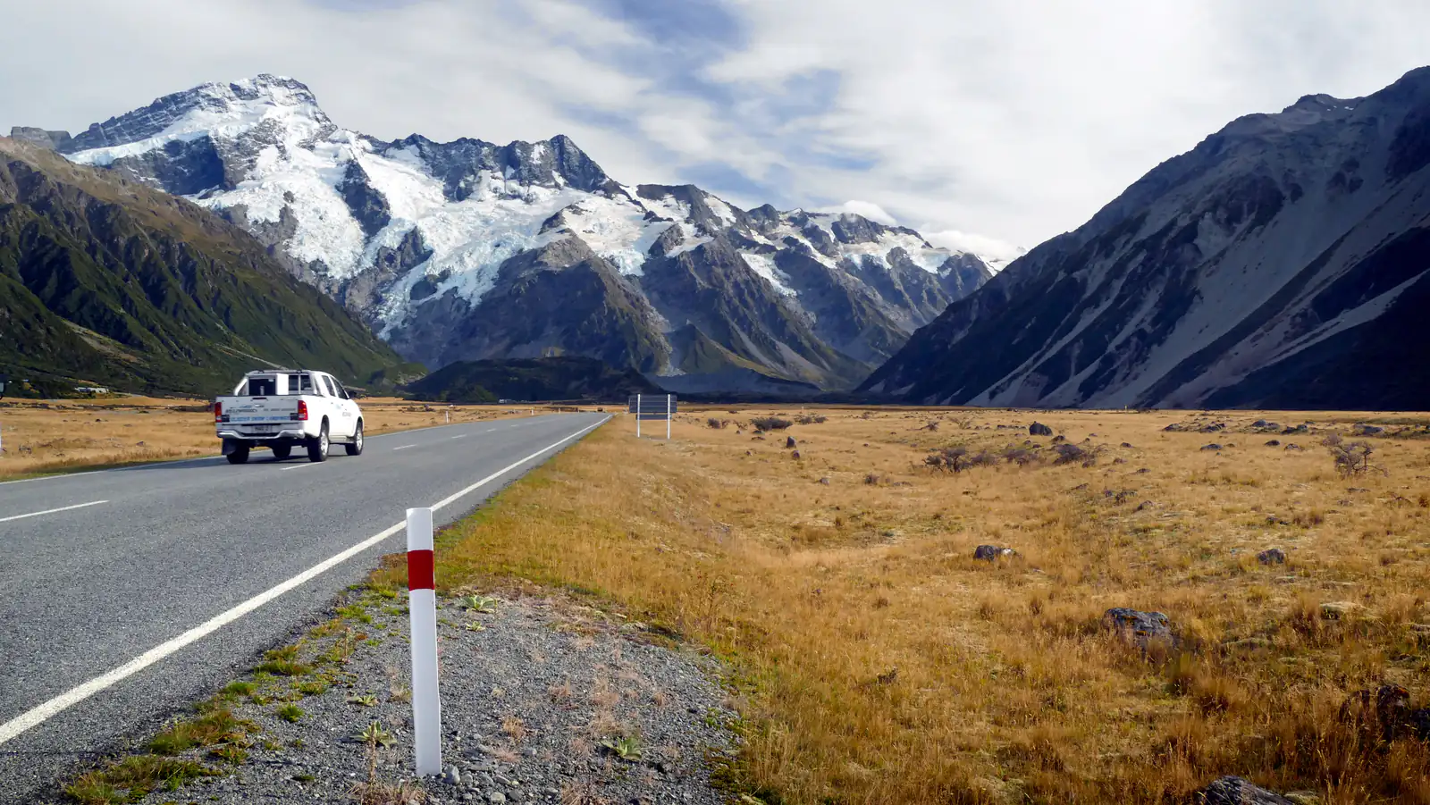 An open road through golden grassland toward snowy mountains