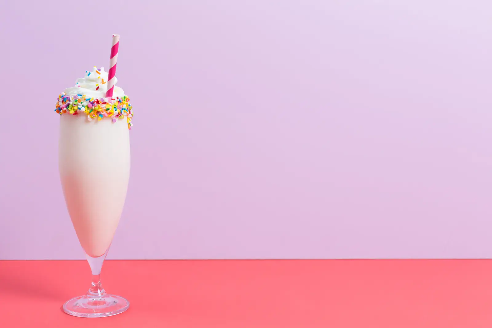 A sprinkle-topped milkshake on a pink and lilac background