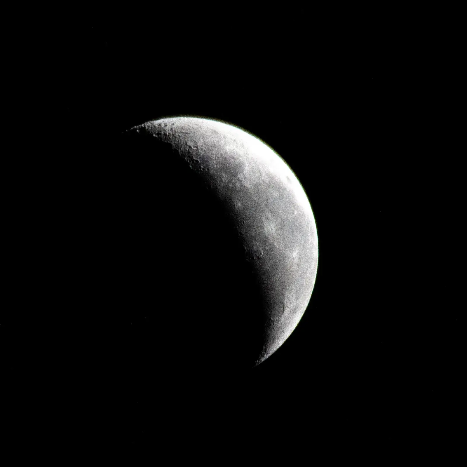 Photograph of a thin waning crescent Moon against black space, taken from the International Space Station