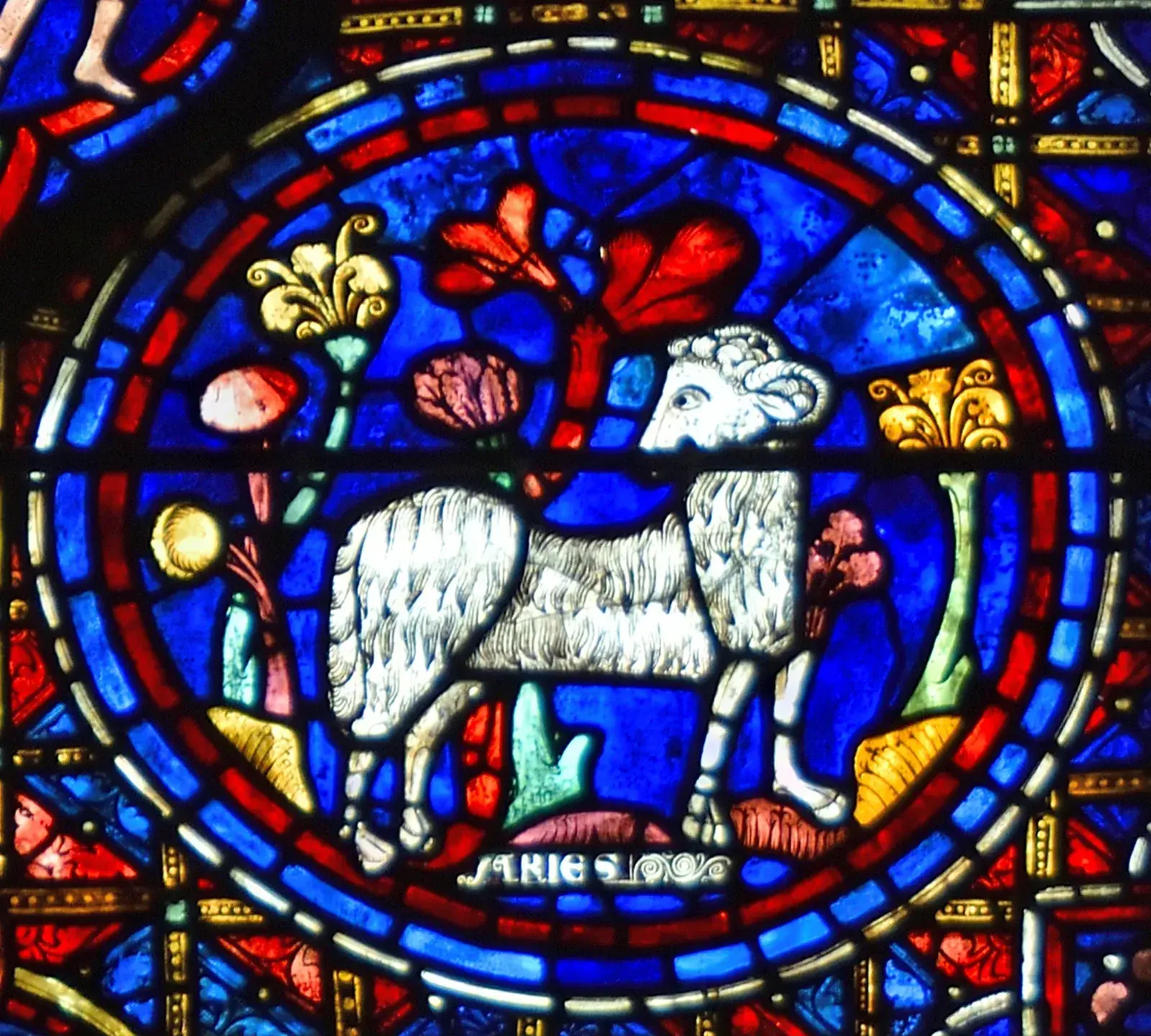 Stained-glass roundel of a white ram among red and yellow flowers, labelled ARIES