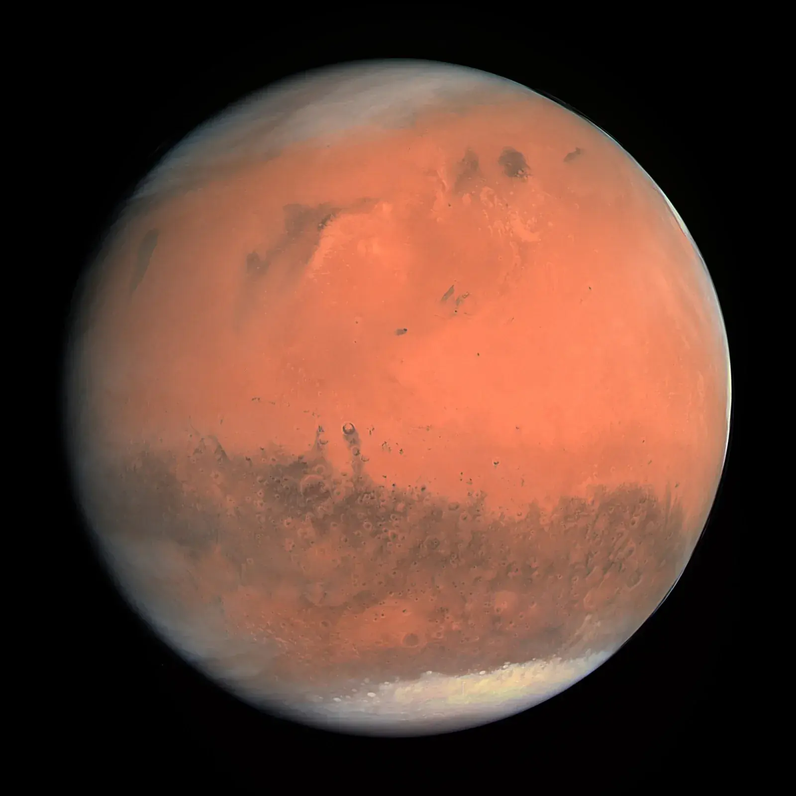 Mars as a rust-orange globe with dark surface markings and a pale polar cap at the bottom, against black space